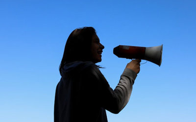 Frau mit Megafon; Bild: Juliana Romão auf Unsplash