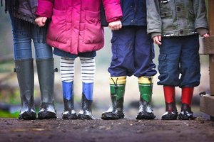 4 Kinder stehen in einer Reihe. Sie haben Wintersachen und Gummistiefel an und stehen draußen. Das Bild zeigt ihre Beine und einen Teil der Oberkörper.